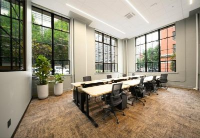 Open-plan workspace with multiple desks, black ergonomic chairs, and large industrial windows.