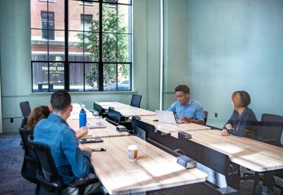 Team meeting at a long wooden desk beside a large window overlooking the street.