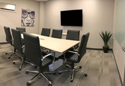 Meeting room with a long white table, black leather chairs, and a wall-mounted screen.