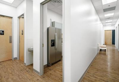 Communal break area hallway featuring a stainless steel refrigerator and light wood flooring.