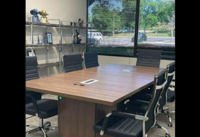 Sunlit conference room with a large wooden table and black executive chairs.