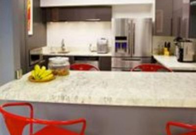 Modern communal kitchen area with stainless steel appliances and red breakfast bar stools.