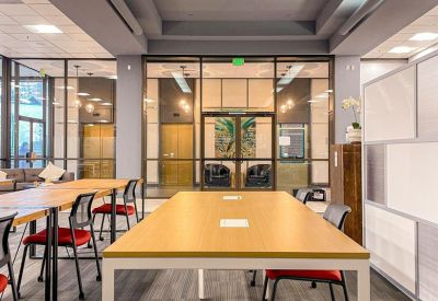 Spacious communal coworking area with long wooden tables, red chairs, and high recessed ceilings.
