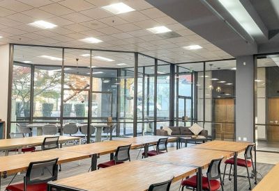 Open-plan office space featuring wooden desks with red chairs and floor-to-ceiling glass partitions.