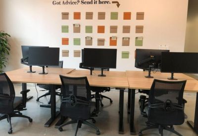 Collaborative workstation area with light wood desks and an advice wall with colorful sticky notes.