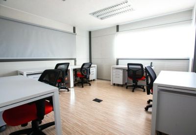 Bright shared office space with white desks and ergonomic chairs with red accents.