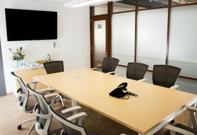 Professional meeting room with a large light wood table and wall-mounted screen.