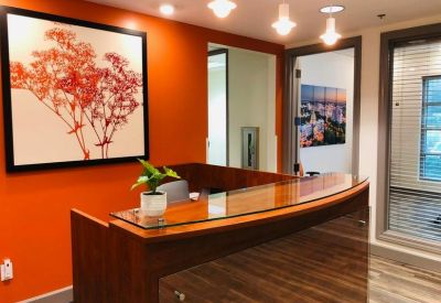 Wooden reception desk in front of an orange wall with floral art and glass doors.