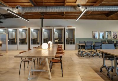 Coworking space with long wooden tables, globe lamps, and private phone booths.