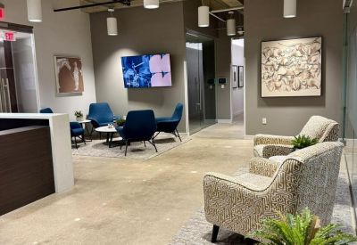Lobby area with industrial ceilings, a reception desk, potted ferns, and comfortable lounge seating.