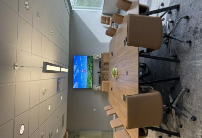 Long wooden boardroom table with tan leather chairs and a wall-mounted TV showing a landscape.