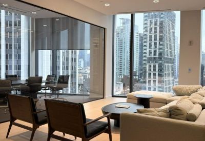Lounge area with a grey sectional sofa and black armchairs overlooking the skyline.