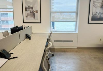 Bright open-plan office workspace with long wooden desks and ergonomic white chairs.