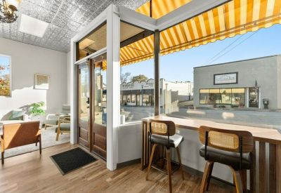 Interior entrance area with window seating, wooden floors, and a view of the street through glass doors.