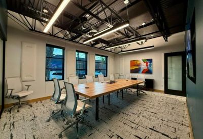 Bright conference room with a large wood table, white mesh chairs, and three vertical windows.