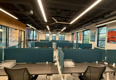 Open-plan office space featuring teal privacy partitions and industrial black ceilings with strip lighting.