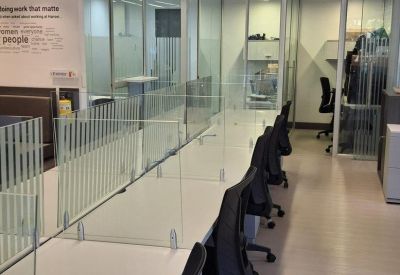 Bright coworking area with long white desks and glass privacy dividers.