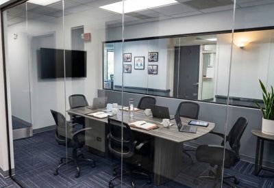 Glass-walled conference room with a grey table, black mesh chairs, and a large monitor.