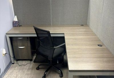 L-shaped office desk and ergonomic chair in a carpeted workspace with privacy partitions.