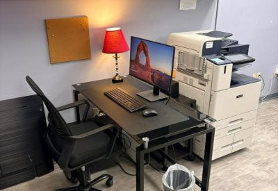 Private workstation with a computer, desk lamp, and large office printer under wall-mounted cabinets.