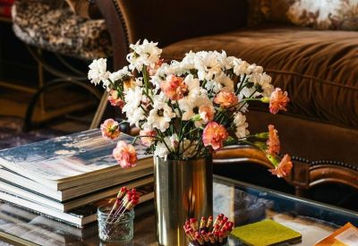 Close-up of a glass coffee table with fresh flowers and stacks of art books next to a velvet armchair.