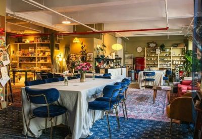 Eclectic open-plan studio featuring multiple dining tables, blue seating, and vibrant rugs.