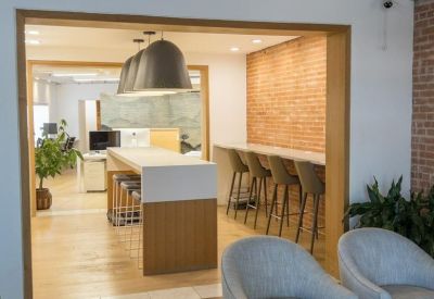 Bright reception lounge with grey armchairs leading into an open-plan office space.