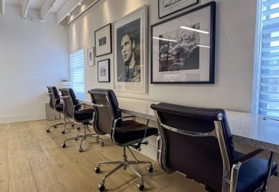 Sleek row of modern black office chairs along a white desk with portrait art.