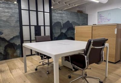 Minimalist square meeting table with two black ergonomic chairs and abstract wall art.