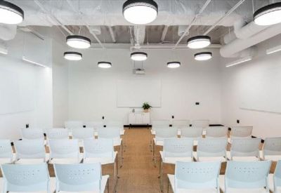 Bright auditorium-style meeting room with white chairs and circular ceiling lights.