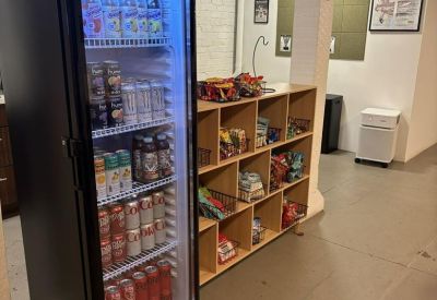 Self-service snack station with a glass-front beverage fridge and wooden cubby shelves.
