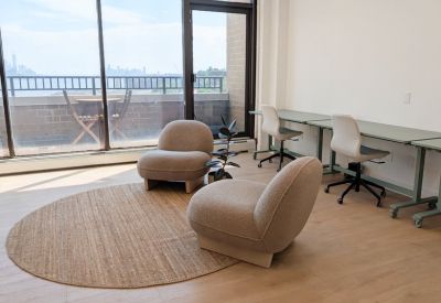 Coworking space featuring lounge seating, a round jute rug, and workstations by a large window.