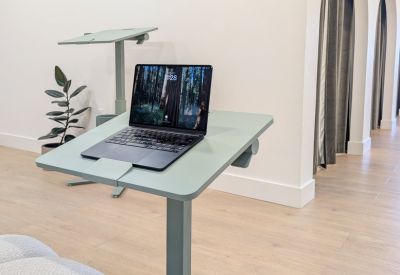 Modern standing desk with a laptop and a view of private office pods.