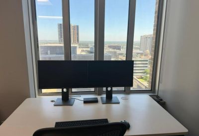 Private office workstation with dual monitors and city views through large windows.
