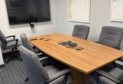 Six-person meeting room with a wooden table, wall-mounted screen, and maritime maps.