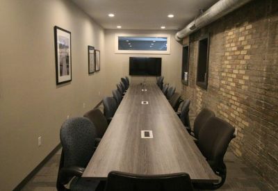 Long conference room with a wooden table, exposed brick wall, and wall-mounted TV.