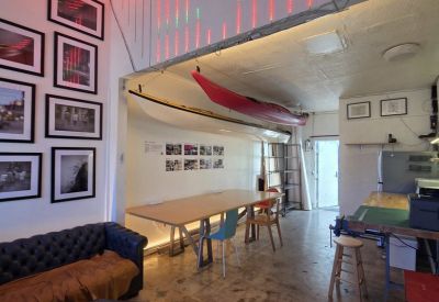 Lounge area with a leather sofa, hanging kayaks, and artistic red and green wall lighting.