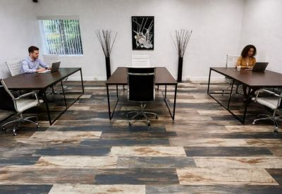 Bright coworking area with several dark wood tables and decorative tall vases with greenery.