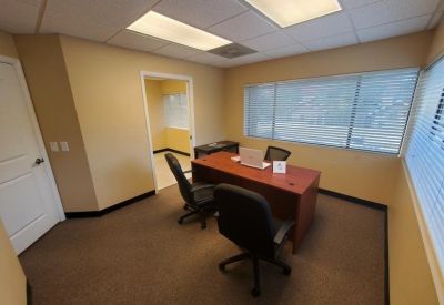 Private office suite with a wood-finished desk, two guest chairs, and large windows with blinds.