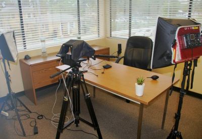 Video production setup in an office with a teleprompter, tripod, and professional lighting equipment.