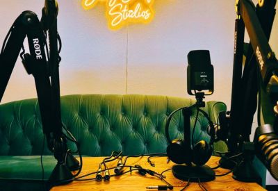 Professional podcast studio setup with high-end microphones and a green velvet sofa under a neon sign.