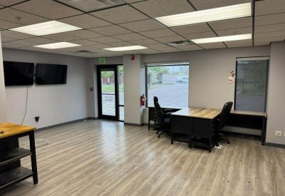 Open office area featuring a desk with two chairs, dual wall-mounted monitors, and a glass entrance door.