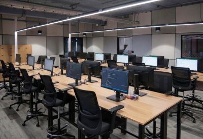 Modern open-plan workspace with rows of wooden desks and ergonomic black chairs.