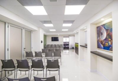 Spacious waiting area with several rows of grey chairs and a wall-mounted art piece.
