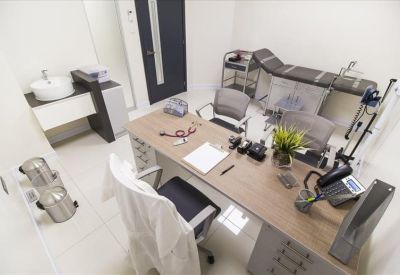 Consultation room with a wooden desk, doctor's chair, and medical examination bed.