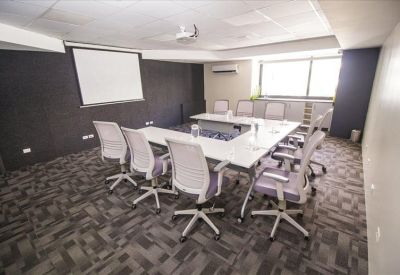 Meeting room with a U-shaped white table, ergonomic chairs, and a projection screen.