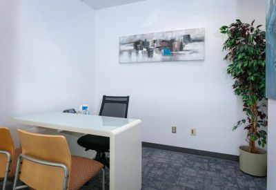 Private office suite with a white desk, orange guest chairs, and a potted tree.