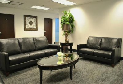 Reception waiting area with black leather sofas and a warm decorative wall hanging.