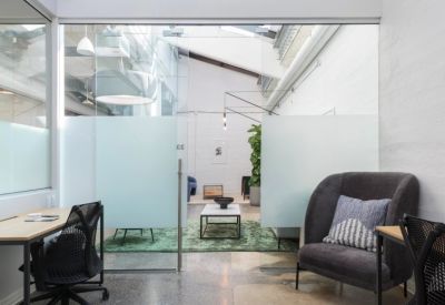 Bright office suite with glass walls, ergonomic desk, and a plush gray armchair.
