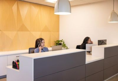 Modern reception desk with two staff members and a geometric wood feature wall.